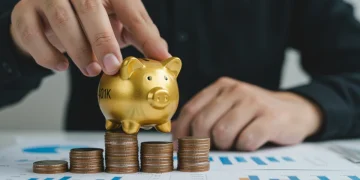 Hand placing piggy bank on coins, symbolizing 401(k) growth and retirement savings maximization.
